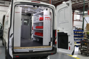 White commercial van with back door open with Weather Guard custom shelving and plastic bins inside parked at workstation White commercial van with back door open with Weather Guard custom shelving and plastic bins inside parked at workstation