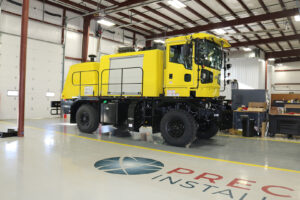 Oshkosh Product H – Series vehicle parked inside workstation with partial Precision Installations logo in show room area Oshkosh Product H – Series vehicle parked inside workstation with partial Precision Installations logo in show room area