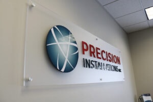 Precision Installations Logo hanging on wall in lobby area Precision Installations Logo hanging on wall in lobby area